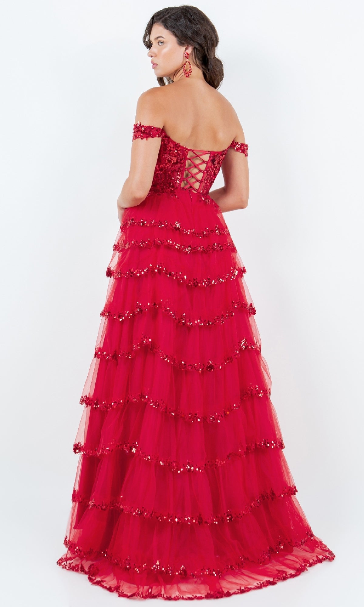 A woman models the Ruffle Prom Ball Gown: Cinderella Couture 8228J—a floor-length red off-the-shoulder dress with a lace-up back, ruffled tulle layers, and sparkling sequin embroidery—against a plain background.